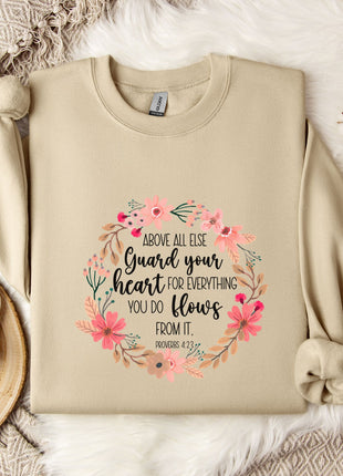 a beige sweatshirt with a floral design and text, along with a coffee mug, a white mug with a heart, and some white flowers on a white fur-covered surface.