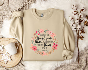 a beige sweatshirt with a floral design and text, along with a coffee mug, a white mug with a heart, and some white flowers on a white fur-covered surface.