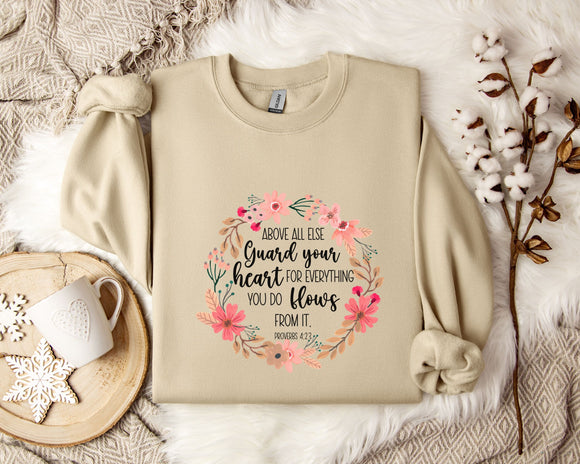 a beige sweatshirt with a floral design and text, along with a coffee mug, a white mug with a heart, and some white flowers on a white fur-covered surface.