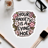 a sticker with the text "Your anxiety is a lying hoe" surrounded by flowers.