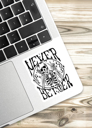 a sticker with a skeleton and the text "NEVER BETTER" on a laptop keyboard.