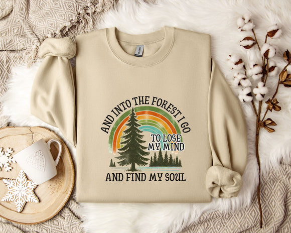 A beige sweatshirt with a graphic design of a forest and a rainbow, along with the text 