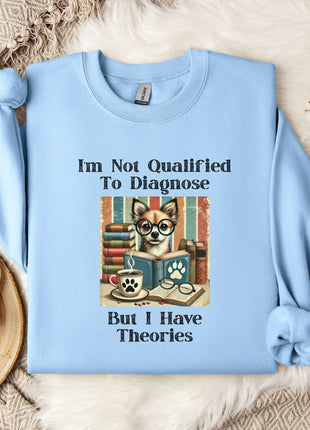 A light blue sweatshirt with a humorous text and an illustration of a cat wearing glasses, placed on a bed with a white blanket and a mug.