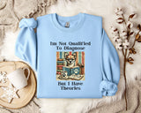 A light blue sweatshirt with a humorous text and an illustration of a cat wearing glasses, placed on a bed with a white blanket and a mug.