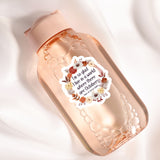 A pink bottle with a floral label, containing a clear liquid, is shown against a white background.