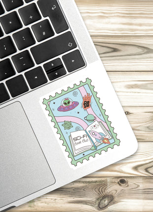 A sticker with a space-themed illustration is placed on the edge of a laptop keyboard.