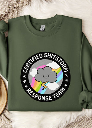 a green sweatshirt with a graphic design on it, placed on a bed with a white blanket and a mug.