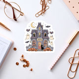 a Halloween-themed sticker of a house with bats, pumpkins, and ghostly figures, surrounded by various office supplies such as a pen, a notebook, and a pair of glasses.