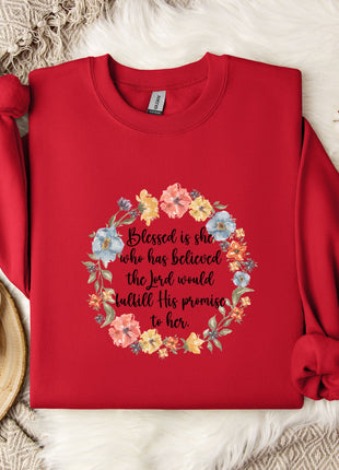 A red sweater with a floral design and a Bible verse printed on it, along with a mug and some white flowers on a white fur rug.