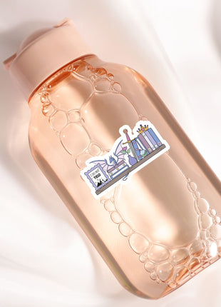 A pink bottle with a sticker on it, placed on a white surface.