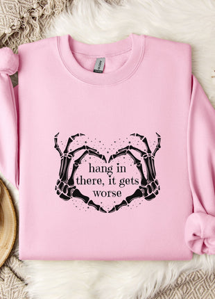 A pink sweatshirt with a graphic design and text printed on it, placed on a white fur-covered surface.