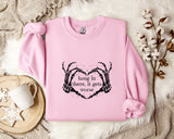 A pink sweatshirt with a graphic design and text printed on it, placed on a white fur-covered surface.