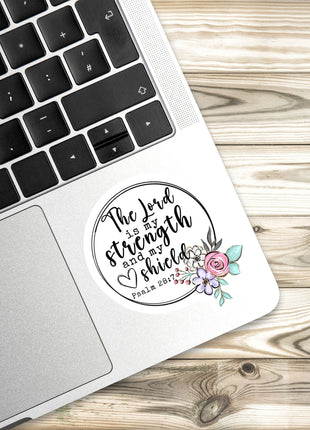 A sticker with a religious quote and a floral design is placed on the side of a laptop keyboard.