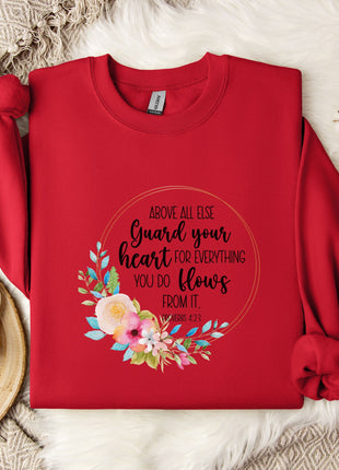 a red sweater with a floral design and text printed on it, placed on a white fur rug. There is also a white mug and a branch of cotton flowers nearby.