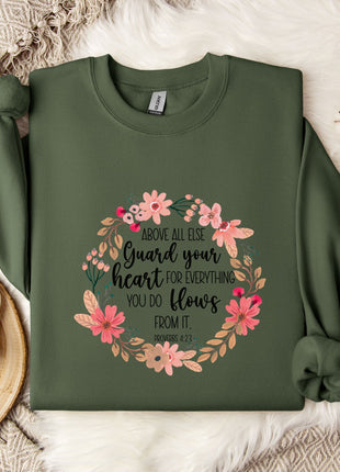 a green sweatshirt with a floral design and text, placed on a bed with a white blanket and a white mug.