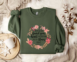 a green sweatshirt with a floral design and text, placed on a bed with a white blanket and a white mug.