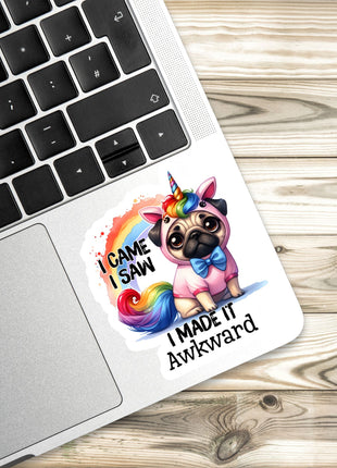 A sticker with a pug dog wearing a unicorn hat and the text "I CAME I SAW I MADE IT AWKWARD" is placed on a laptop keyboard.