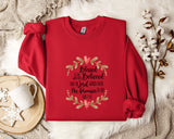 A red sweater with a floral design and text printed on it, along with a mug, a white mug, and some white flowers on a white fur rug.