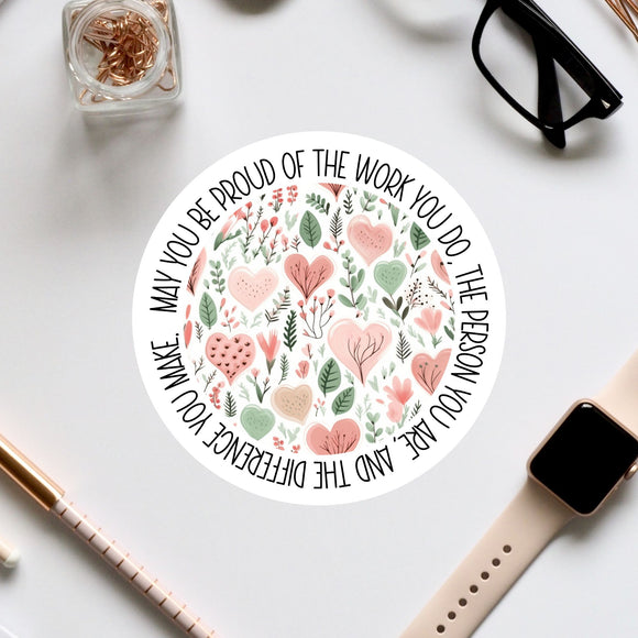 a round sticker with a floral design and text, surrounded by various office supplies such as a pair of glasses, a watch, and a pen.