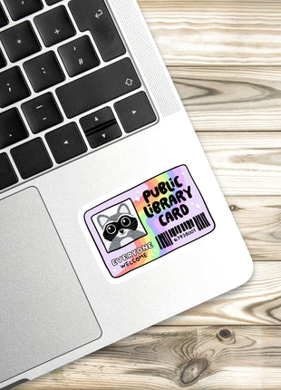 A sticker with a raccoon and the text "Public Library Card" is placed on the side of a laptop keyboard.