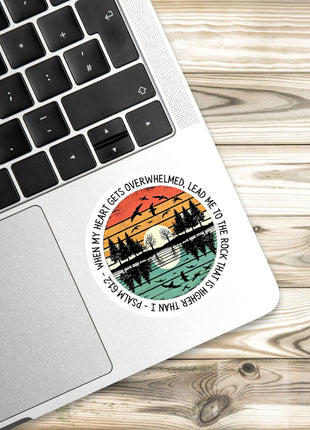 A sticker with a sunset and silhouetted trees design is placed on the edge of a laptop keyboard.