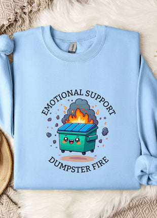 A light blue sweatshirt with a graphic design depicting a trash can on fire, surrounded by flames and smoke, along with the text "Emotional Support Dumpster Fire".