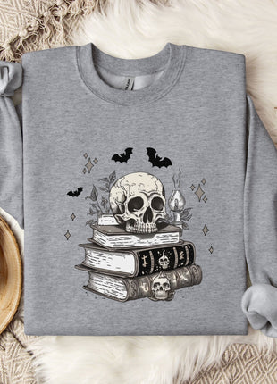 a gray sweatshirt with a skull and bats design, along with a stack of books and a mug on a bed with a white blanket.