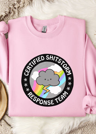 a pink sweatshirt with a graphic design on it, placed on a bed with a white blanket and a mug.