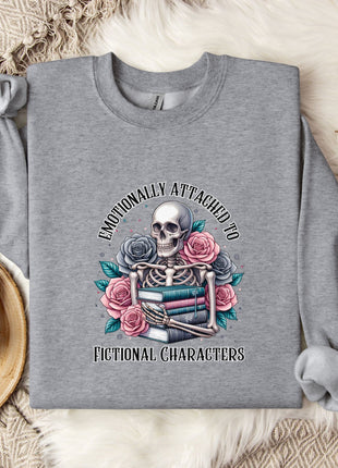 a gray sweatshirt with a graphic design of a skeleton holding a book and flowers, accompanied by the text "Emotionally Attached to Fictional Characters".