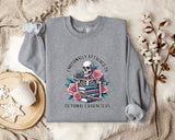a gray sweatshirt with a graphic design of a skeleton holding a book and flowers, accompanied by the text "Emotionally Attached to Fictional Characters".