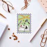 a postage stamp with a cartoon illustration of a book club, a magnifying glass, and various crime-related items, surrounded by office supplies such as pens, paper clips, and a notebook.