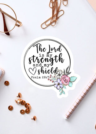 a sticker with a quote from the Bible verse Psalm 28:7, surrounded by various office supplies such as pens, a notebook, and a pair of glasses.
