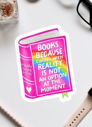 a sticker with a book and a quote about coping with reality, surrounded by various office supplies and a pair of glasses.