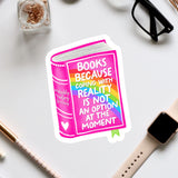 a sticker with a book and a quote about coping with reality, surrounded by various office supplies and a pair of glasses.