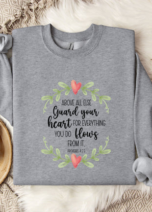 a gray sweatshirt with a printed message, a mug, and some flowers on a bed with a blanket.
