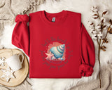 A red sweater with a colorful seashell and starfish design, along with a mug and a white flower, is displayed on a white fur rug.