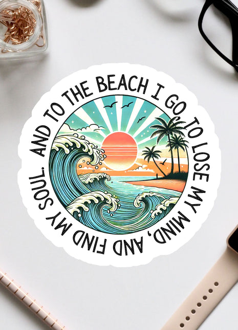 A sticker with a beach scene and a sunset, surrounded by various office supplies and a pair of glasses.