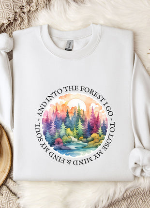 A white sweatshirt with a colorful forest scene design, along with a mug, a snowflake, and some branches, all placed on a white fur rug.