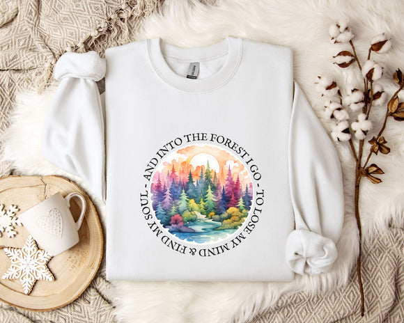 A white sweatshirt with a colorful forest scene design, along with a mug, a snowflake, and some branches, all placed on a white fur rug.