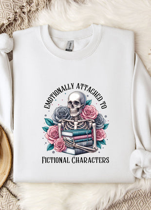 a white sweatshirt with a graphic design of a skeleton holding a book and flowers, surrounded by the text "Emotionally Attached to Fictional Characters".
