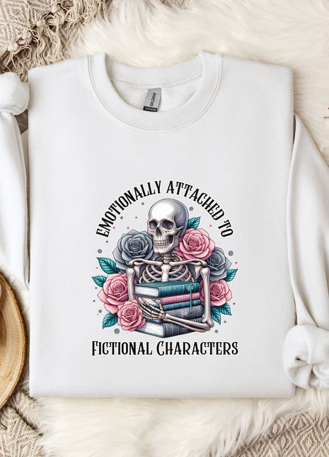 a white sweatshirt with a graphic design of a skeleton holding a book and flowers, surrounded by the text "Emotionally Attached to Fictional Characters".