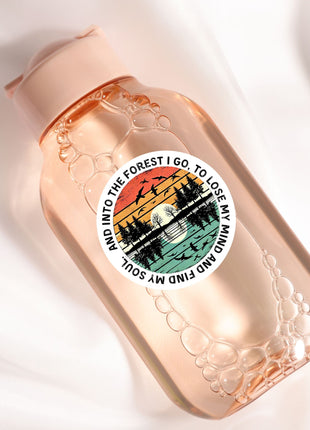 A pink bottle with a sticker featuring a sunset landscape and silhouettes of trees.