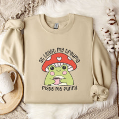 a beige sweatshirt with a mushroom character and text printed on it, along with a mug and some flowers on a bed.