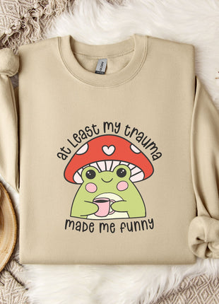 a beige sweatshirt with a mushroom character and text printed on it, along with a mug and some flowers on a bed.