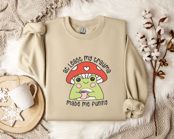 a beige sweatshirt with a mushroom character and text printed on it, along with a mug and some flowers on a bed.