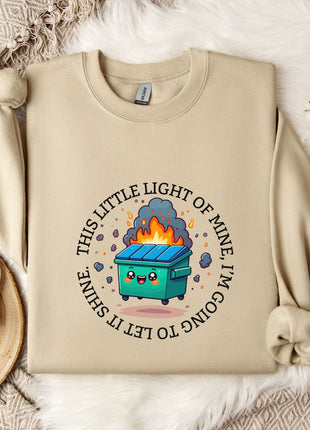 a beige sweatshirt with a graphic design depicting a trash can with flames coming out of it, surrounded by a circular design with the text "This little light of mine is going to blow up".