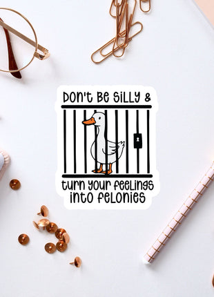 a sticker with a cartoon duck inside a cage, surrounded by various office supplies such as a pen, a notebook, and a pair of glasses.