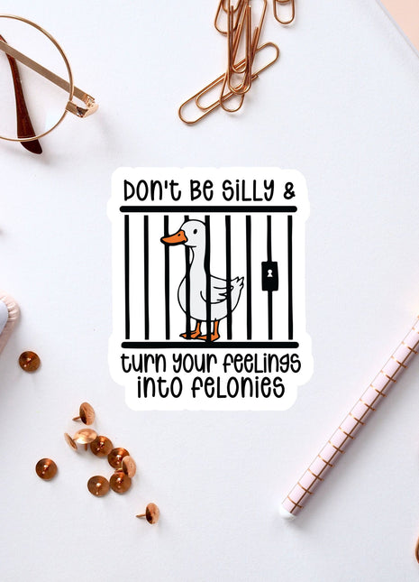 a sticker with a cartoon duck inside a cage, surrounded by various office supplies such as a pen, a notebook, and a pair of glasses.