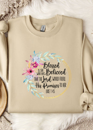 A beige sweatshirt with a floral design and text printed on it, along with a coffee mug and some white flowers on a bed.