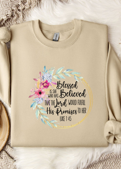 A beige sweatshirt with a floral design and text printed on it, along with a coffee mug and some white flowers on a bed.